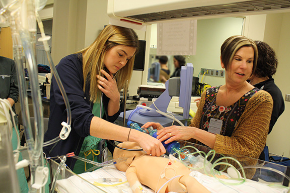 Two people are seen standing over a dummy simulating a patient.