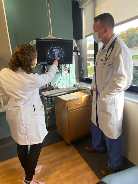 Katherine Pavlos, PA-C, at left, points to a CT scan image on a screen while Ed Stene, AGACNP-BC, looks at the screen.