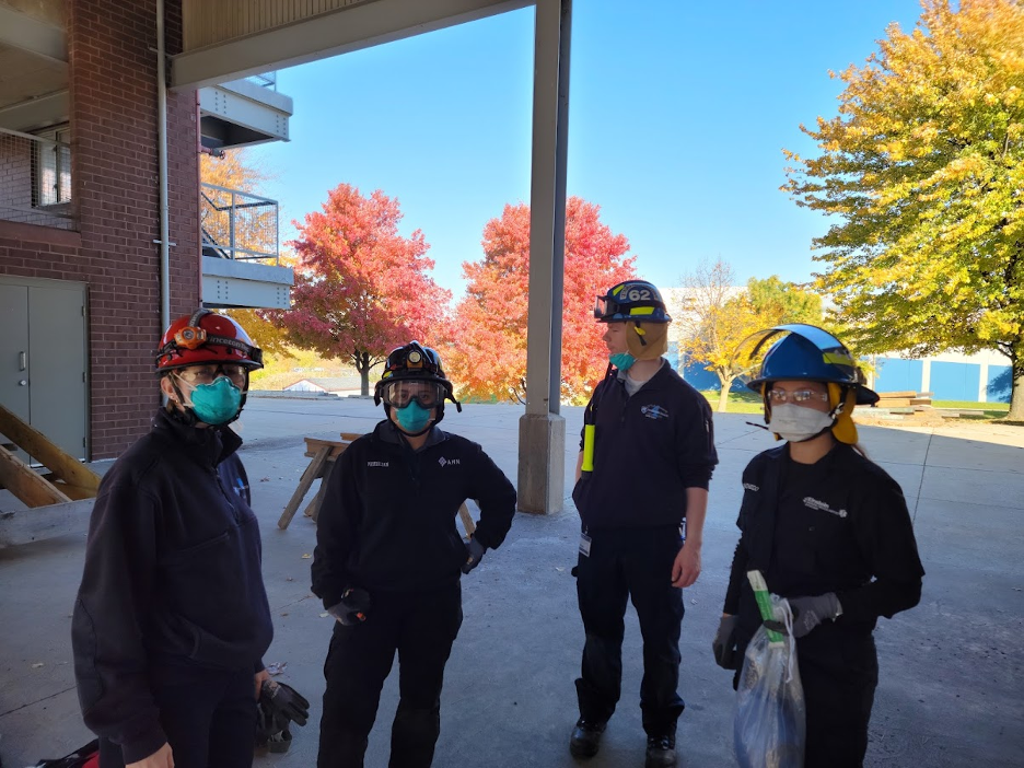 Four EMS Fellowship trainees stand in a building, wearing blue uniforms, protective helmets and face masks.