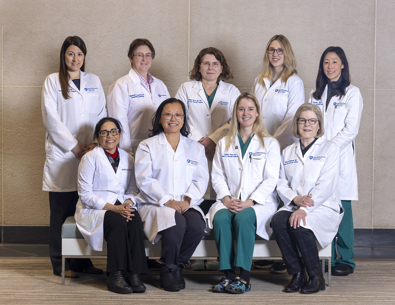 Nine women cardiologists in white coats; four seated in front and five standing in the back.