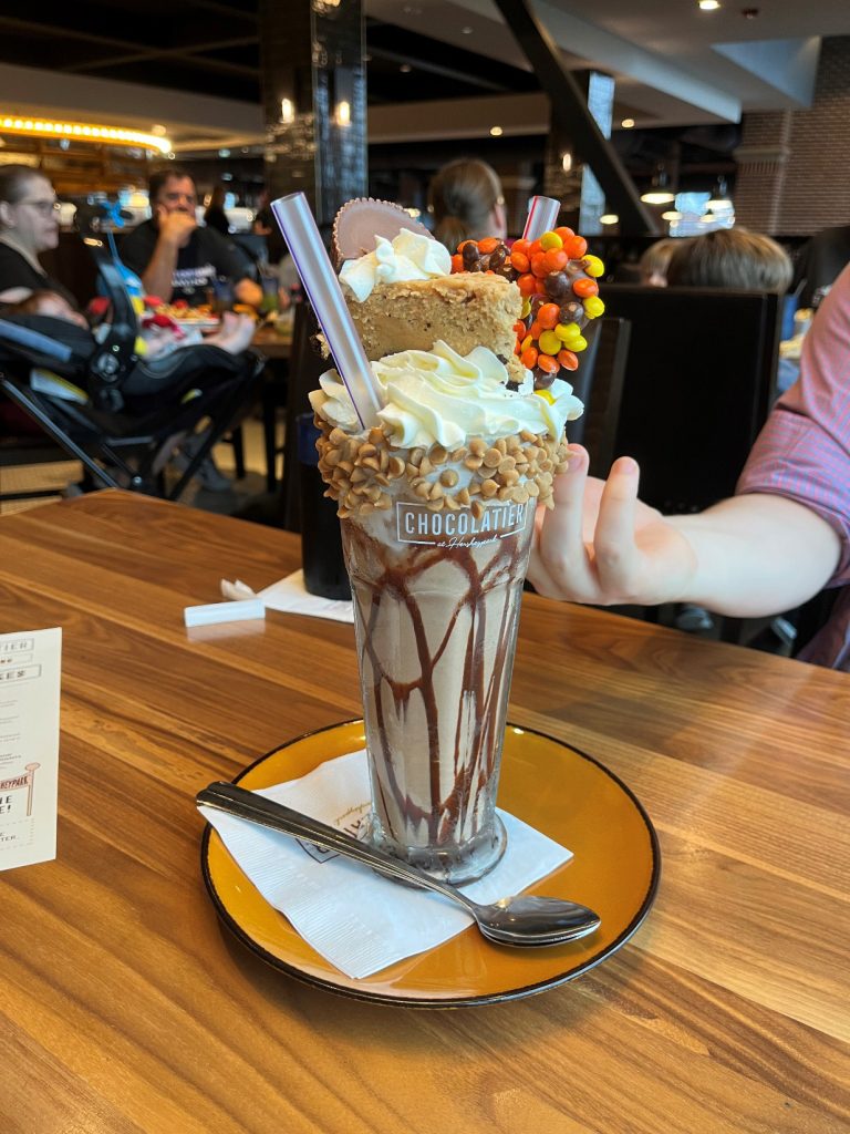 Deluxe chocolate sundae in a tall glass includes ice cream, chocolate syrup, Reese's Pieces, peanut butter chips, whipped cream and more.
