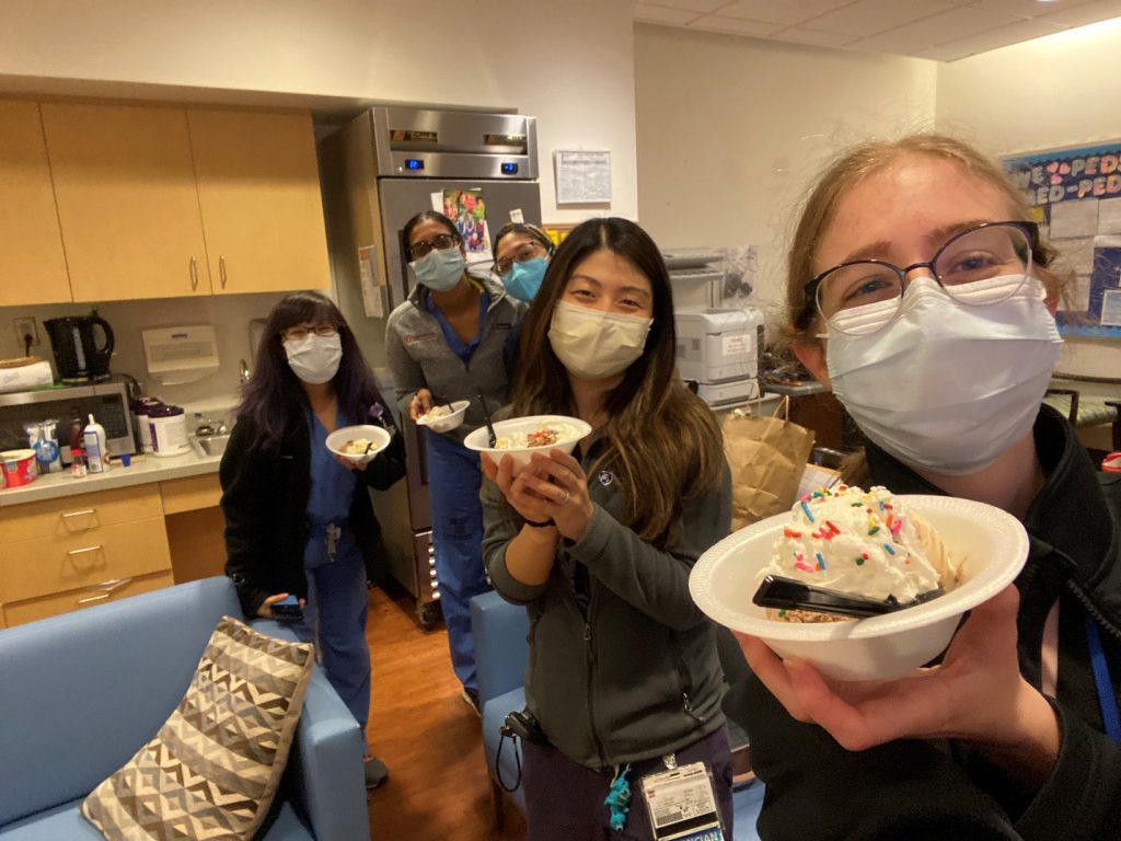 Five residents wearing face masks hold up dishes of ice cream in the resident lounge.