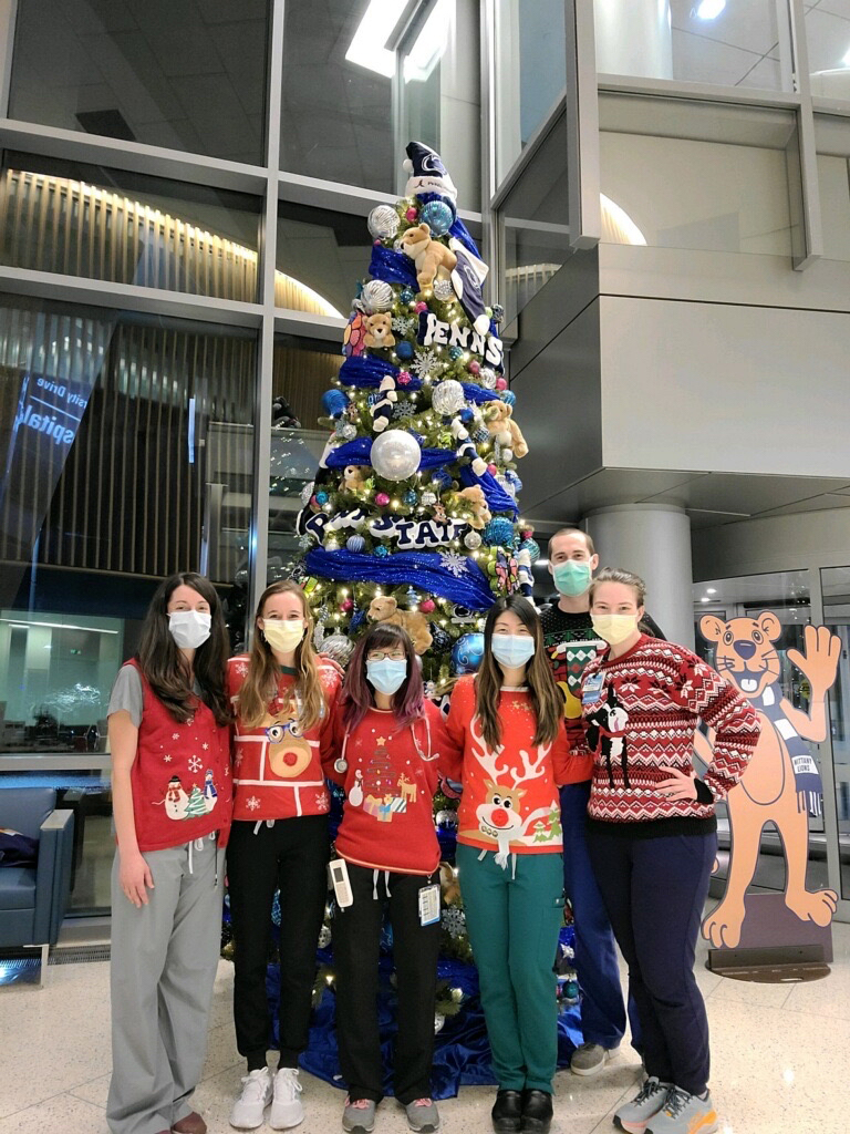Six residents wearing Christmas sweaters and face masks pose in front of a Christmas tree.