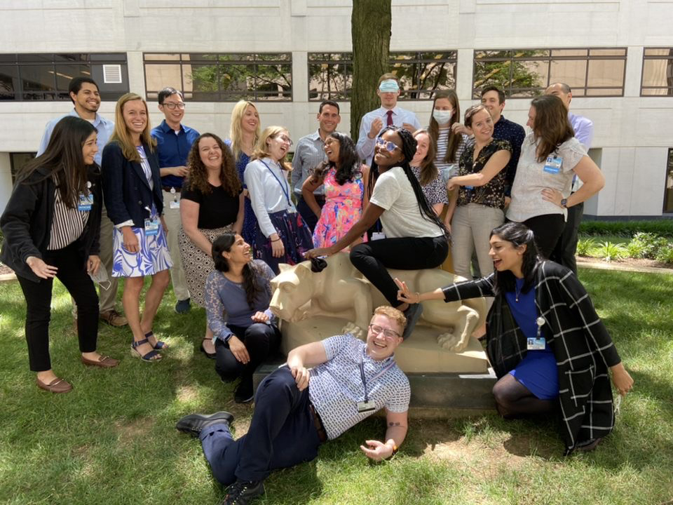 A group of residents pose with the Nittany Lion statue at Penn State College of Medicine, including one resident sitting on the lion