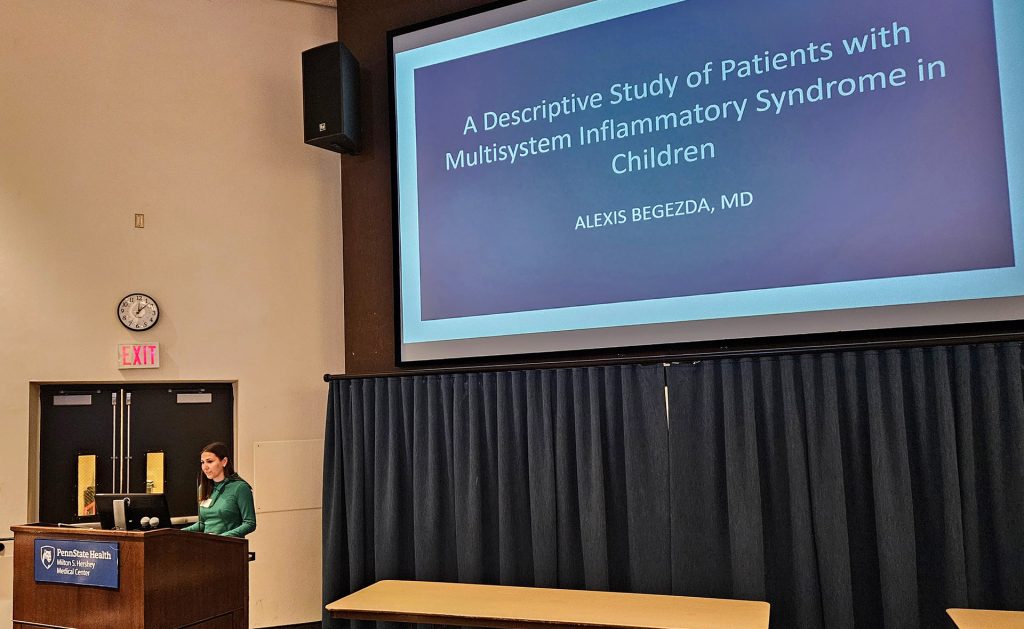 Alexis Begezda stands behind a lectern while a screen behind her shows a slide with the title, A Descriptive Study of Patients with Multisystem Inflammatory Syndrome in Children