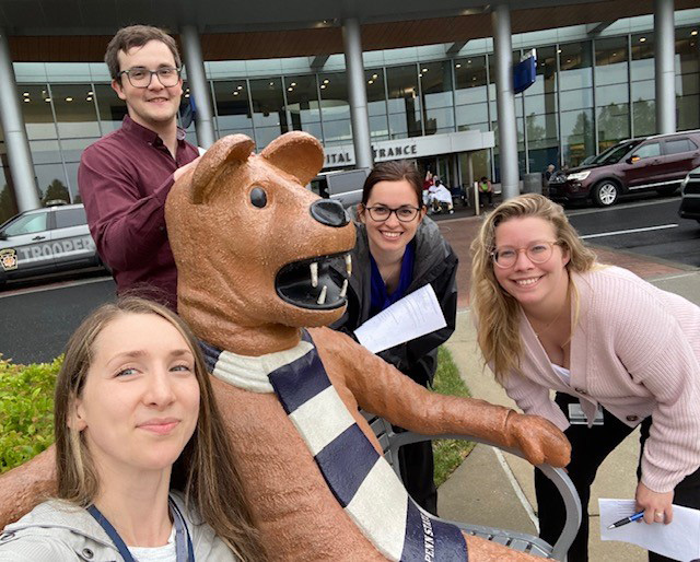 Four people pose around a Nittany Lion statue for a self-style photo.