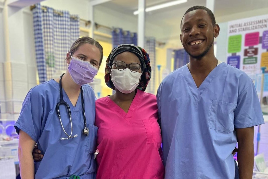 Emily Gibbons poses with a woman in the middle and a man on the right, all wearing medical scrubs; Gibbons and the woman are wearing face masks and Gibbons has a stethoscope around her neck.