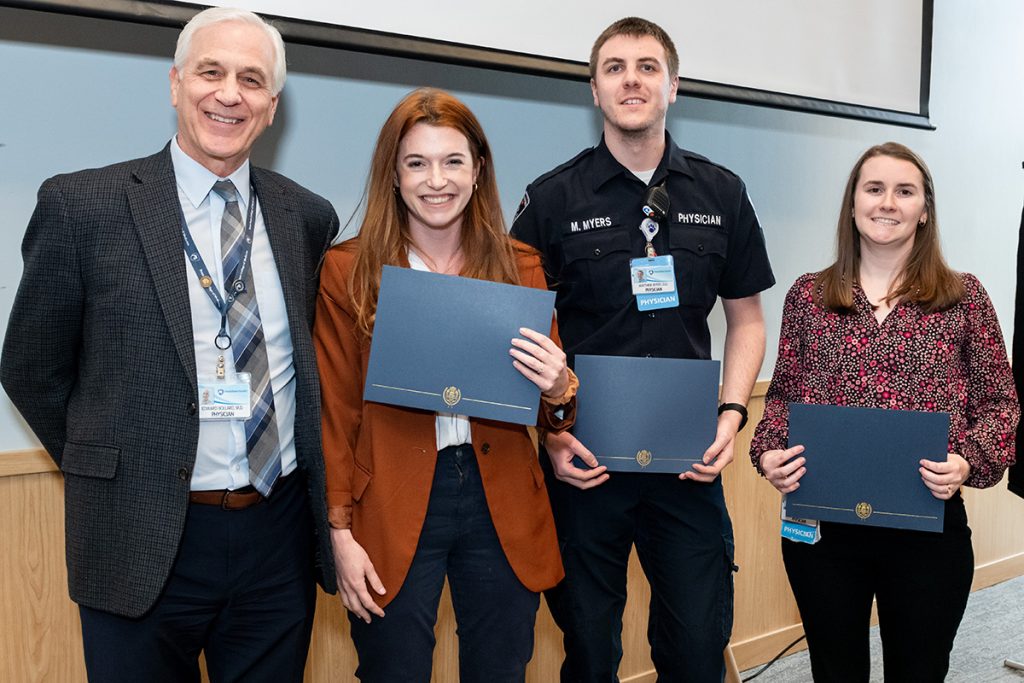 Four people lined up by a wall; the three on the right are holding up awards