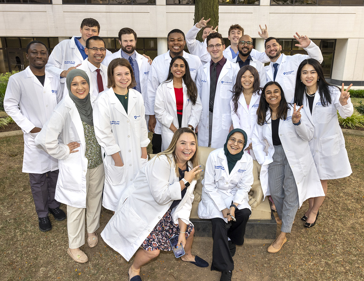 A group of residents wearing white coats making a fun pose around a Nittany Lion statue in the College of Medicine courtyard