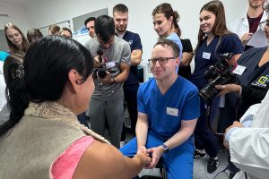 Dr. Scott Walen, seated in front of other physicians and a cameraman, holds the hand of a woman seated in front of him